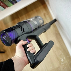 Der Vistefly V15 Max wird mit einer Fugendüse entlang einer weißen Fußleiste geführt. Holzspäne liegen auf dem Boden.