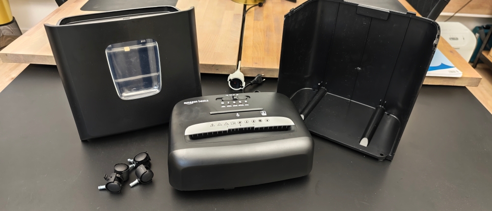 Ein schwarzer Amazon Basics Aktenvernichter liegt auseinandergebaut auf einem Tisch.