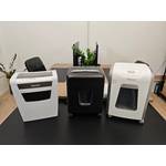 Drei Aktenvernichter von Leitz, Amazon Basics und Fellowes stehen auf einem schwarzen Tisch.