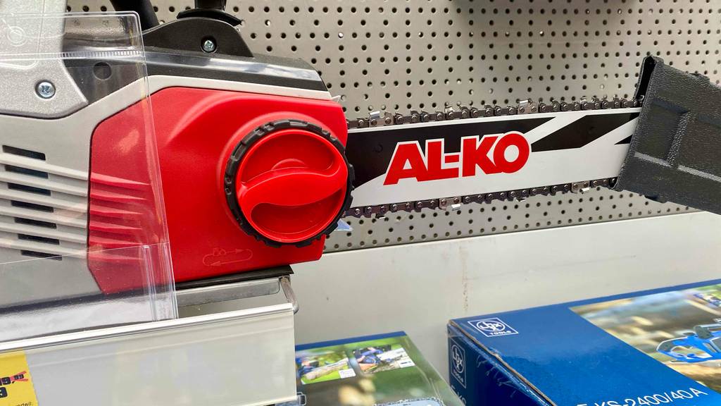 Elektro-Kettensägen-Test: Detailansicht einer roten Feststellschraube zum werkzeuglosen Kettenwechsel von einem Al-Ko Modell in Rot-Grau in einem Verkaufsbereich.