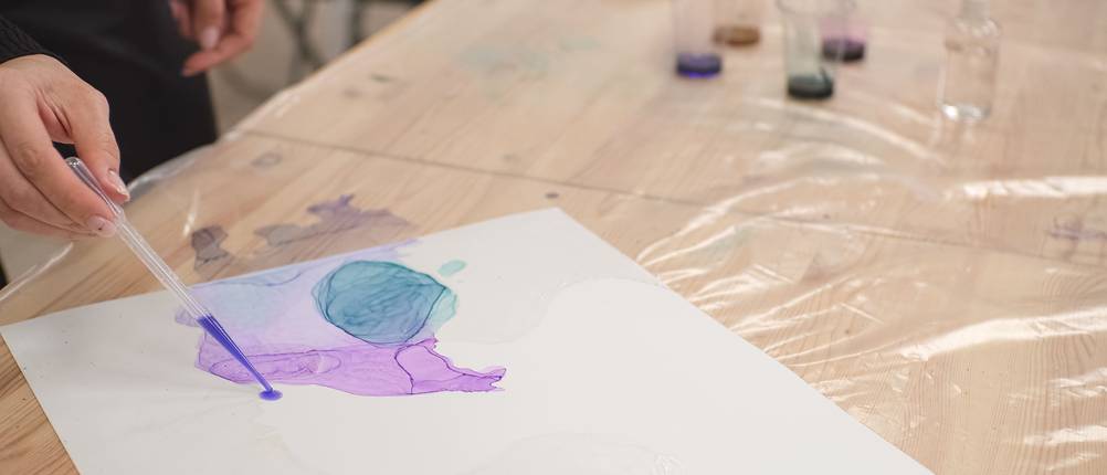 alcohol-ink-test: Frau tropft lila Alcohol Ink mit der Pipette auf ein unfertiges Bild.