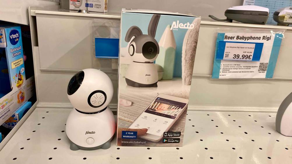 Im Test: Ein Babyphone mit Kamera-App von der Seite neben dem seitlich stehenden Originalkarton auf einer hellen Fläche inklusive Preisangabe im Hintergrund.