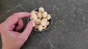 Ansicht von oben auf eine Hand, die eine Macadamia-Nuss im Test aus einer dekorativen Snack-Schale nimmt.