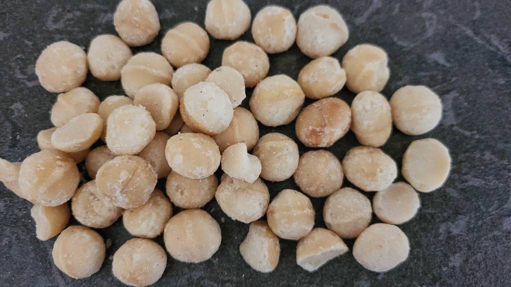 Viele Macadamia-Nüsse im Test liegen auf einer schwarzen Oberfläche.