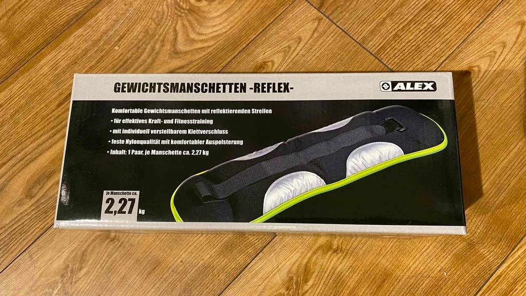 Gewichtsmanschetten von Alex befinden sich in ihrer Verpackung auf einem Holzboden und sind zum Test bereit.