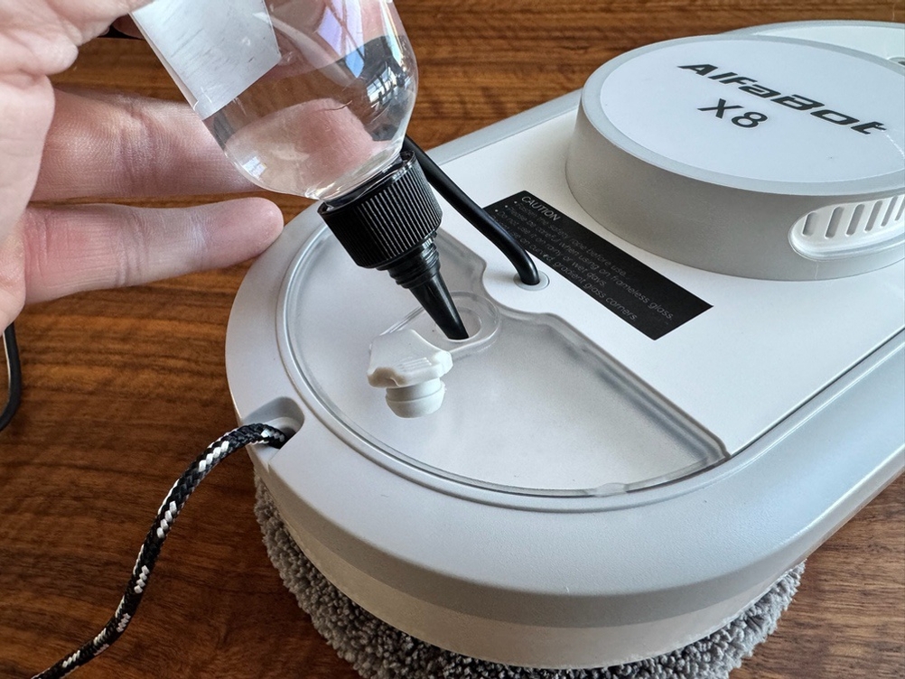 Eine Hand gibt etwas aus einer Flasche in den Alfabot X8