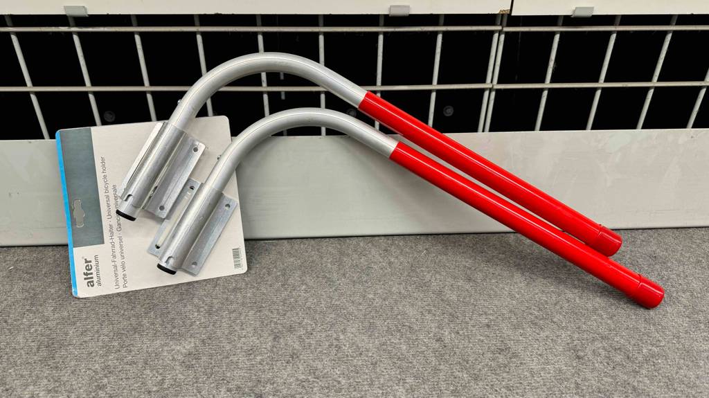 Vor einer Wand lehnt ein Fahrradhalter im Test mit roter Gummi-Beschichtung.