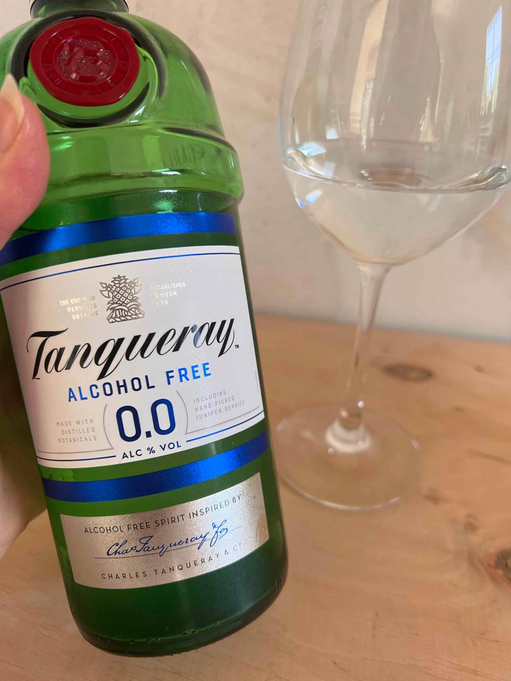 Eine Hand hält eine Flasche alkoholfreien Gins im Test vor ein Weinglas.