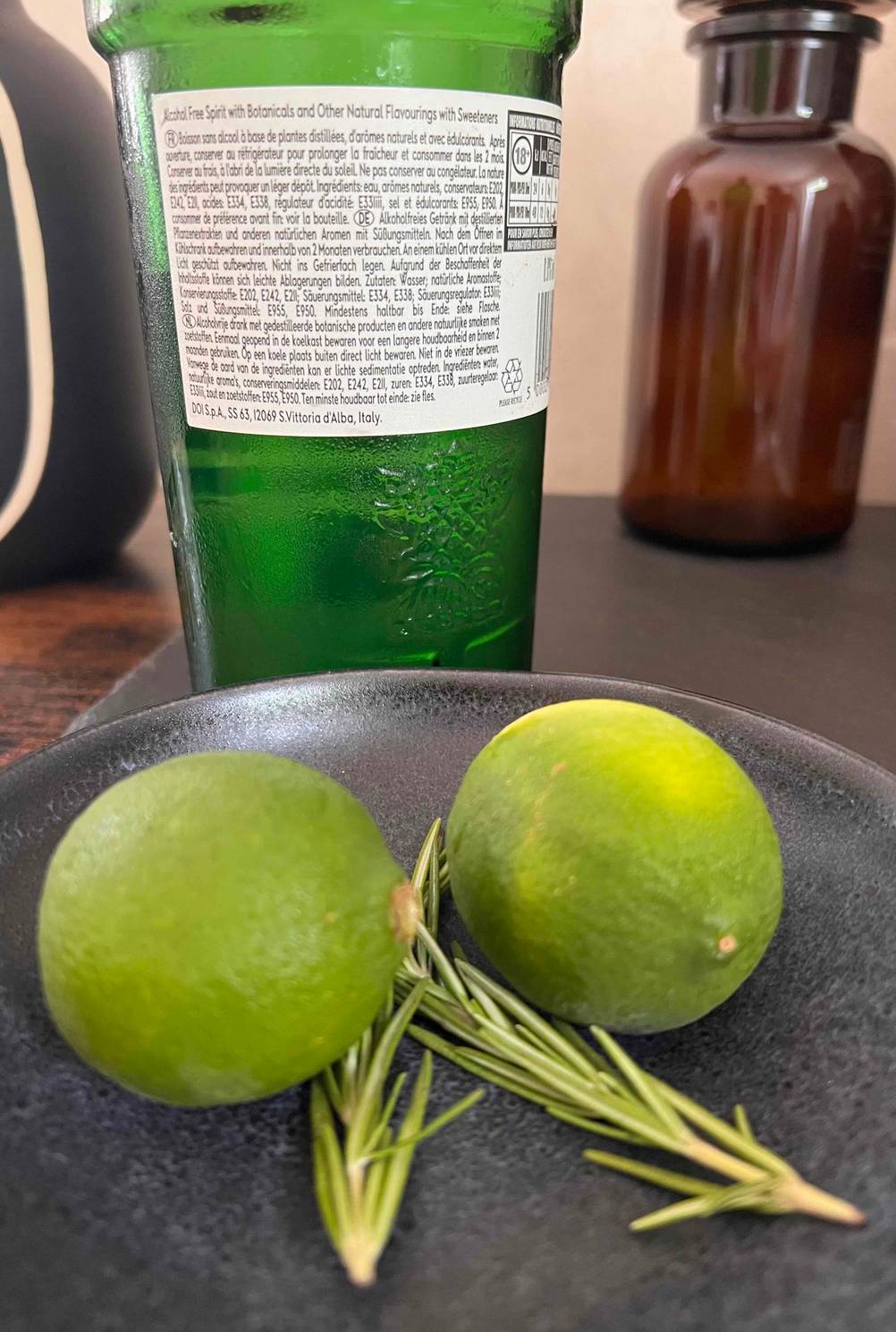 Vor einer Flasche des getesteten alkoholfreien Gins liegen zwei Limetten und Rosmarin.
