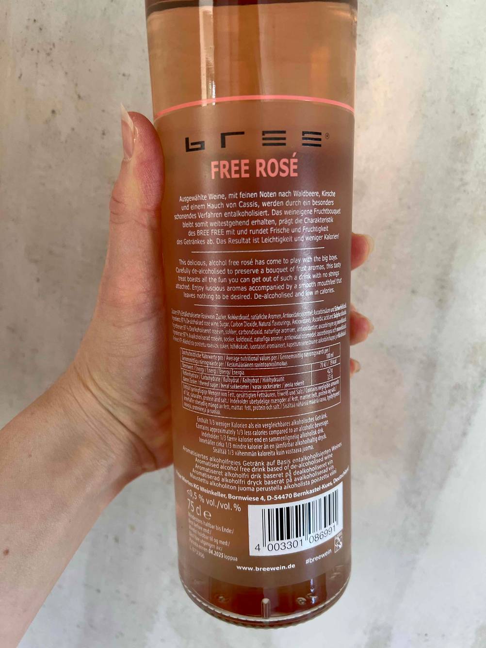 Rückseite einer Flasche des getesteten alkoholfreien Weins von einer Hand vor eine helle Fläche gehalten.