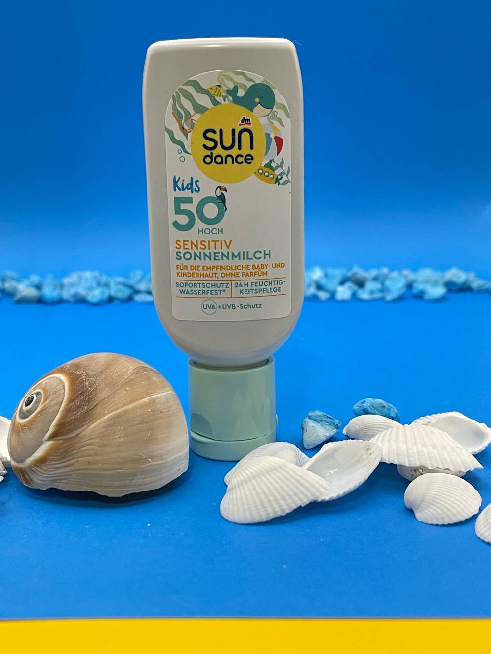 Eine Tube der getesteten Allergie-Sonnencreme auf blauem Untergrund, davor Muscheln.
