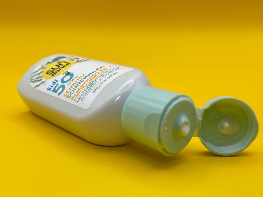 Auf einer gelben Fläche liegt die Allergie-Sonnencreme im Test mit geöffnetem Deckel.