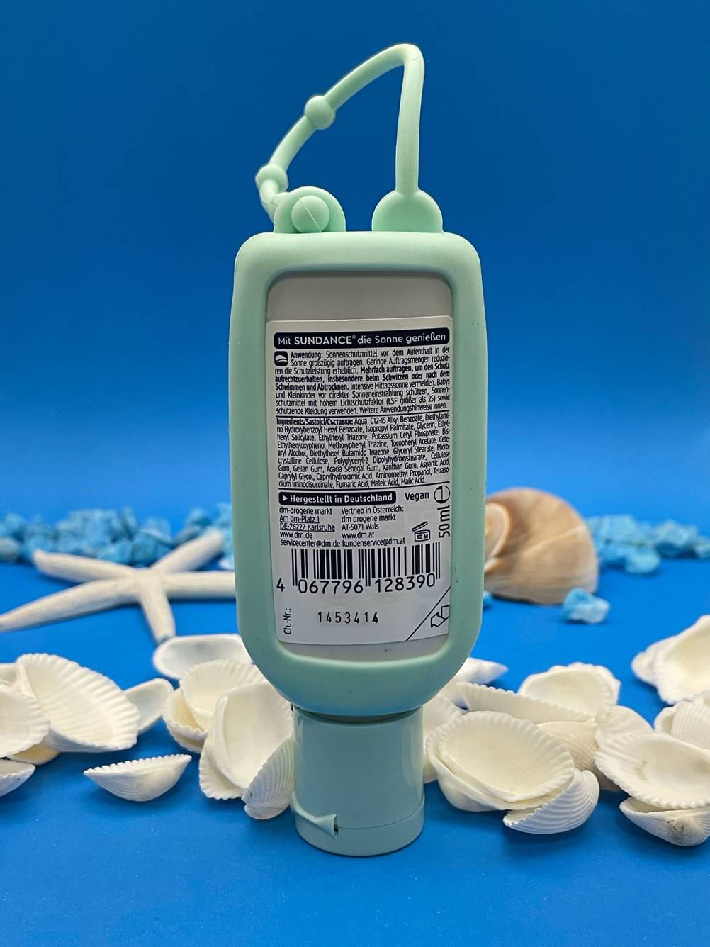 Die getestete Allergie-Sonnencreme mit der Rückseite nach vorne auf einer blauen Fläche mit Muscheln.