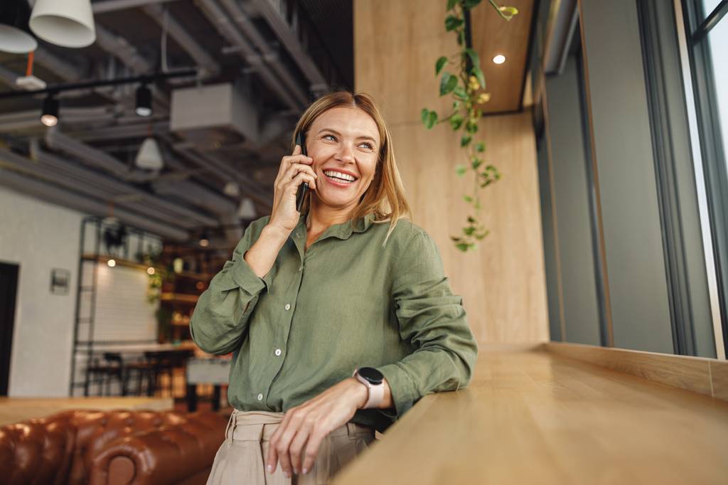 Eine Frau telefoniert an einer Holztheke mit ihrem Smartphone.