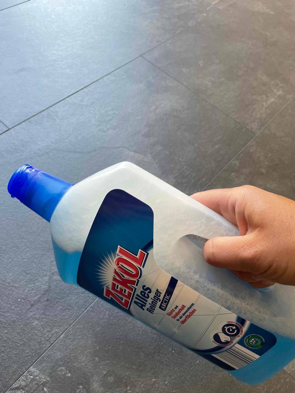 Allzweckreiniger getestet: Eine Hand hält eine Flasche über einen Fließenboden.