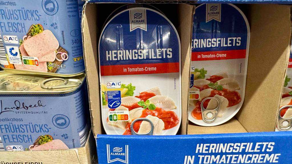 Mehrere Dosen mit Heringen (zum Essen) im Test befinden sich in einem Karton im Verkaufsregal.