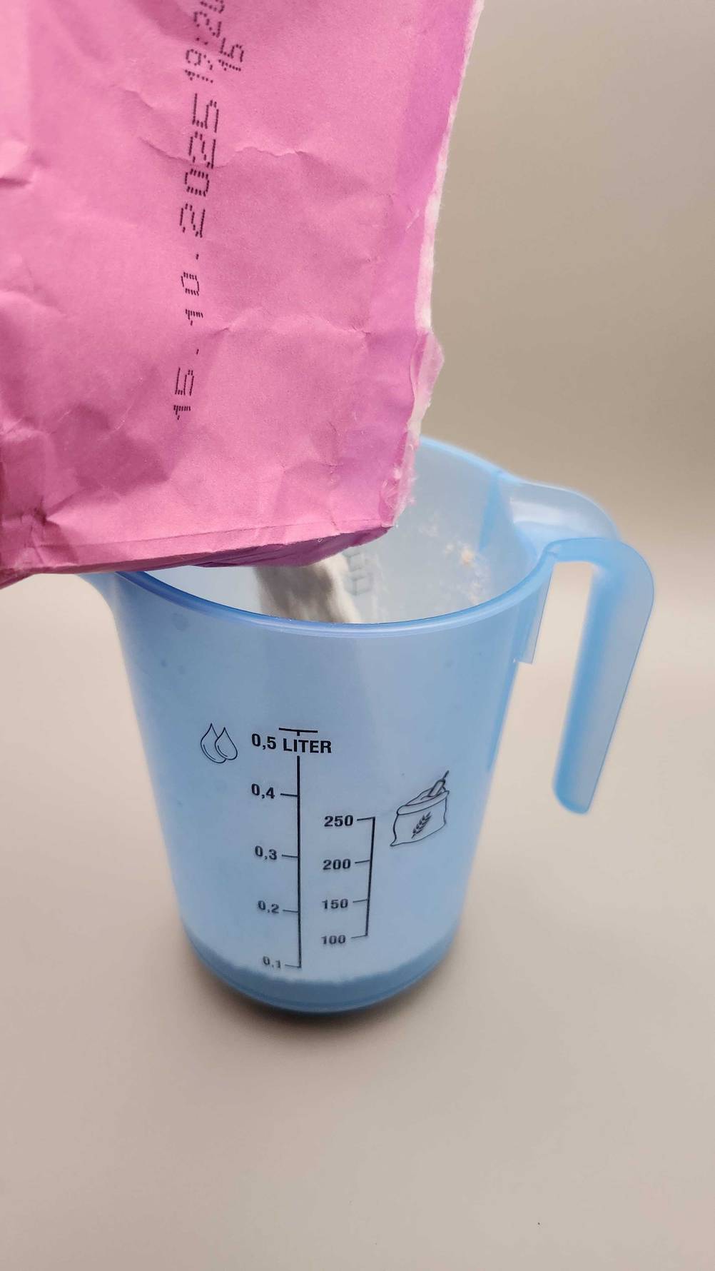 Aus einer Packung wird Buchweizenmehl zum testen in einen Messbecher geschüttet.