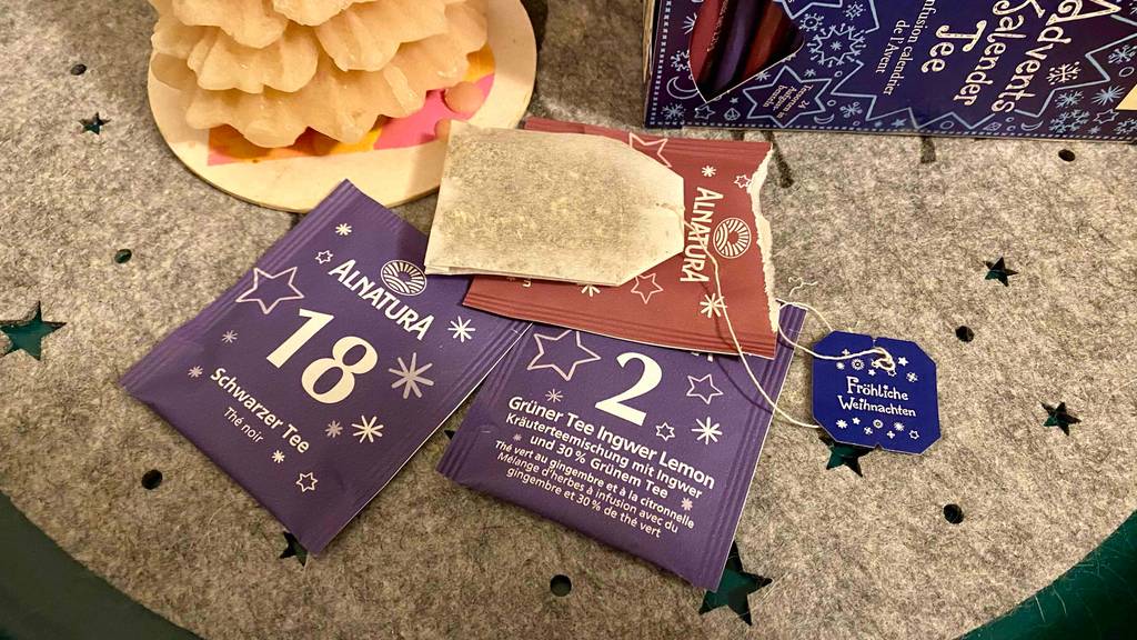 Tee-Adventskalender im Test: Mehrere Teebeutel verpackt und unverpackt liegen neben einer blau-weißen weihnachtlichen Verpackung von Alnatura.