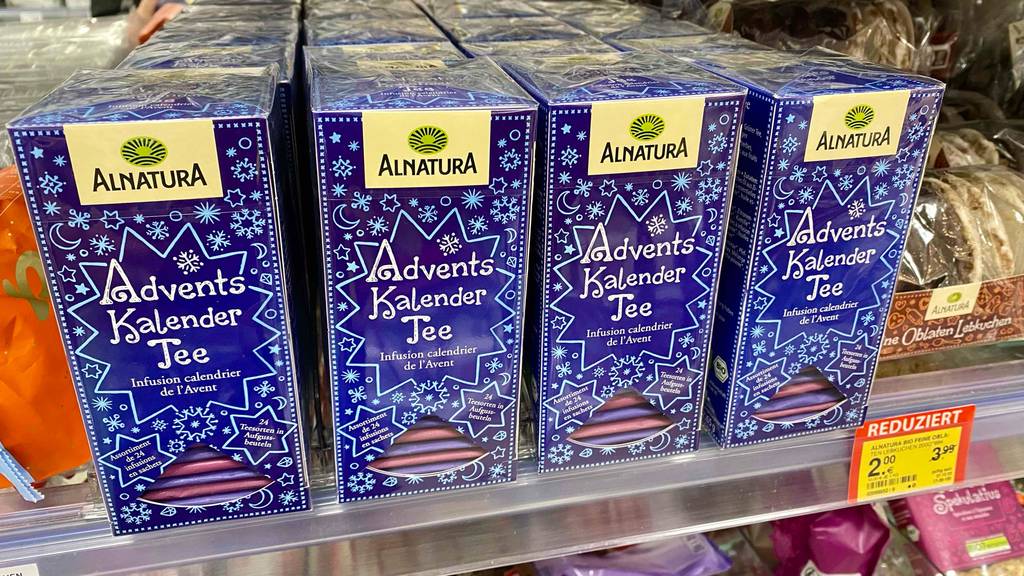Tee-Adventskalender-Test: Mehrere Verpackungen im blau-weißen weihnachtlichen Design mit Alnatura Adventskalender Tee befinden sich inklusive Preisschild in einem Verkaufsregal.