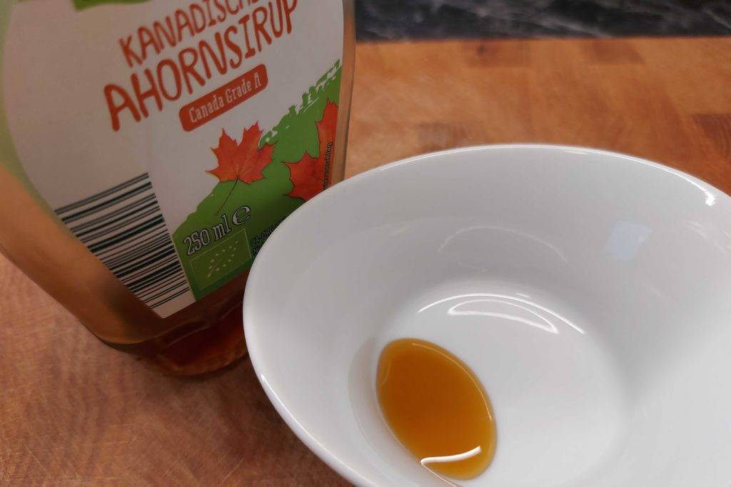 In einer weißen Schale ist etwas Ahornsirup zum testen aus der Flasche, die dahinter steht.