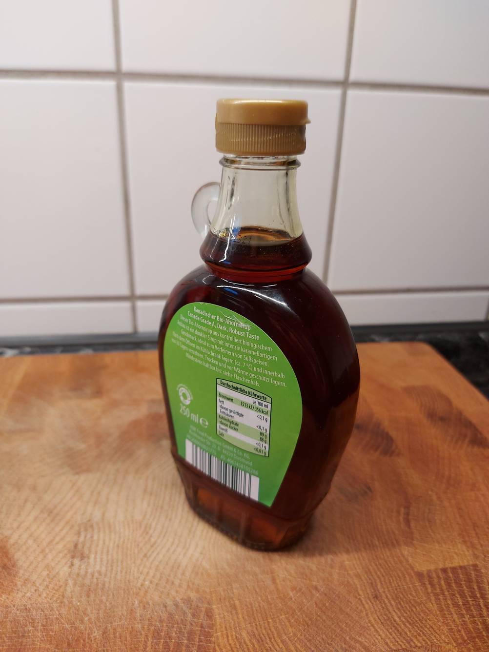 Im Test: Eine Flasche Ahornsirup von Gut Bio steht mit der Rückseite nach vorn auf einer Holz-Küchenarbeitsplatte.
