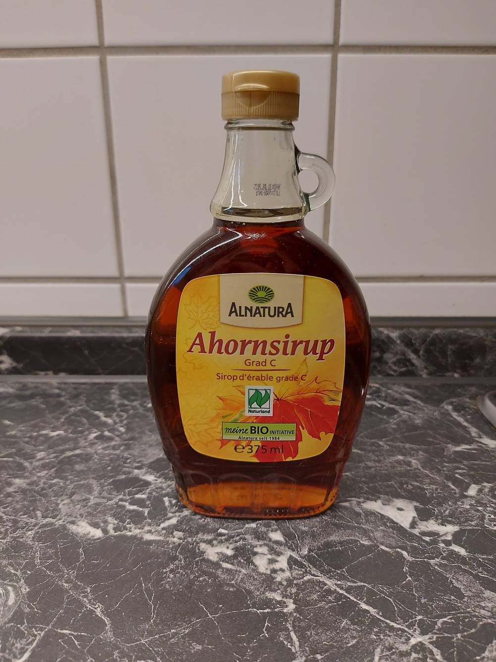 Eine Flasche getesteter Ahornsirup von Alnatura steht auf einer marmorierten Küchenarbeitsplatte.