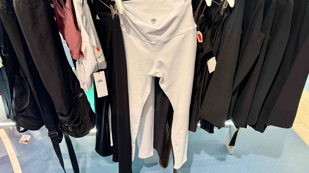 Die weiße Yoga-Pants im Test hängt auf einem Bügel vor schwarzer Bekleidung im Verkauf.