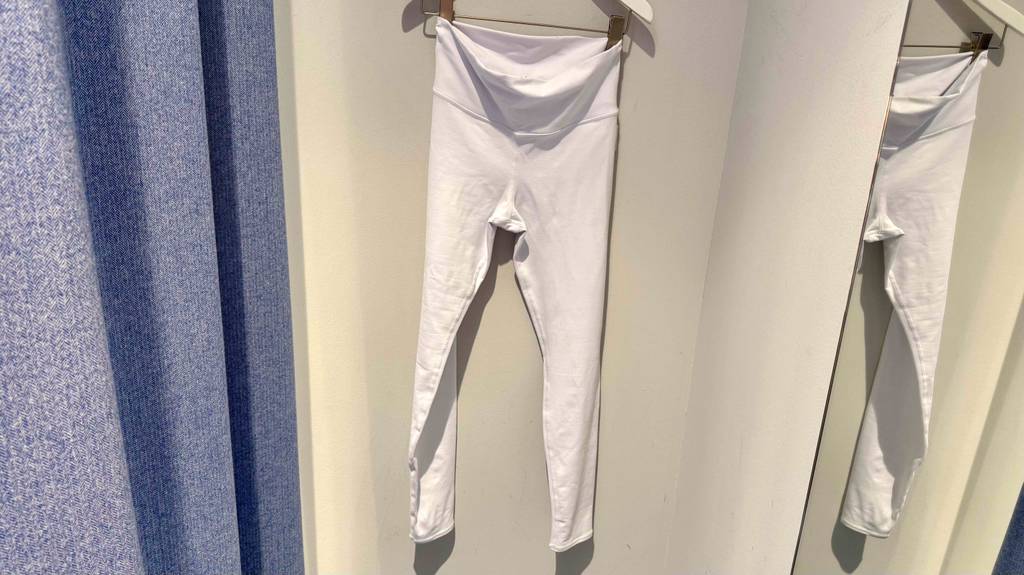 Getestet: Die Yoga-Pants in Weiß mit Hüftbund ohne Gummi hängen auf einem Bügel in einer Ankleidekabine.