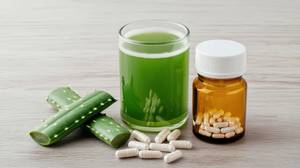 Aloe-vera-Kapseln-Test: Ein Glas grüner Saft steht neben einem Schraubglas mit Kapseln und einem Aloe-vera-Blatt. 