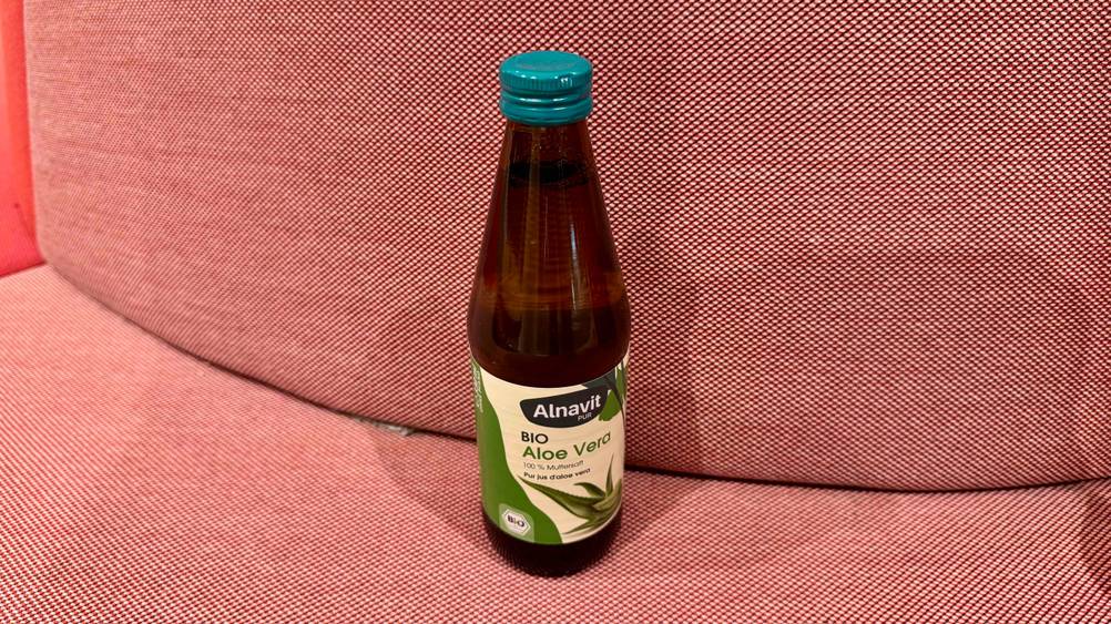 Aloe-vera-Saft (bio) im Test: Eine Flasche von schräg oben auf einem roten Polster.