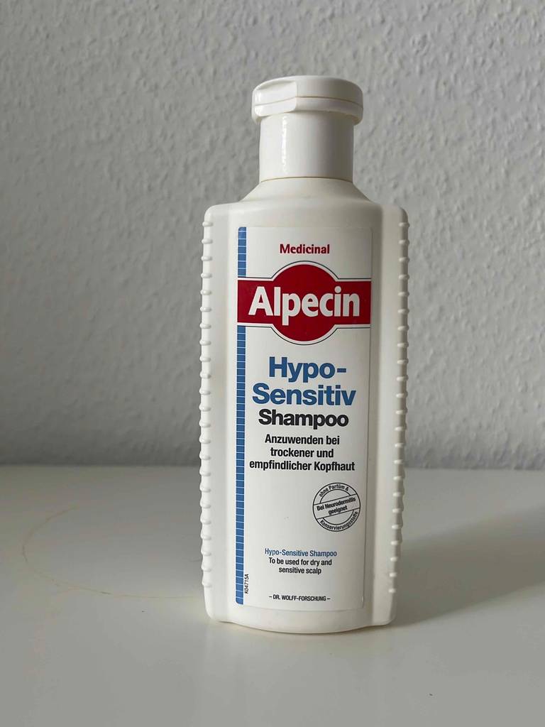 Vordere Gesamtansicht des Haarwassers von Alpecin in einer weißen Kunststoffflasche mit Dosier-Klapp-Verschluss vor hellem Hintergrund.