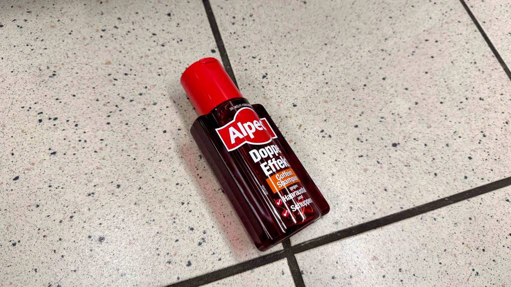 Eine Flasche getestetes Männer-Shampoo gegen Haarausfall liegt auf einem Fliesenboden.