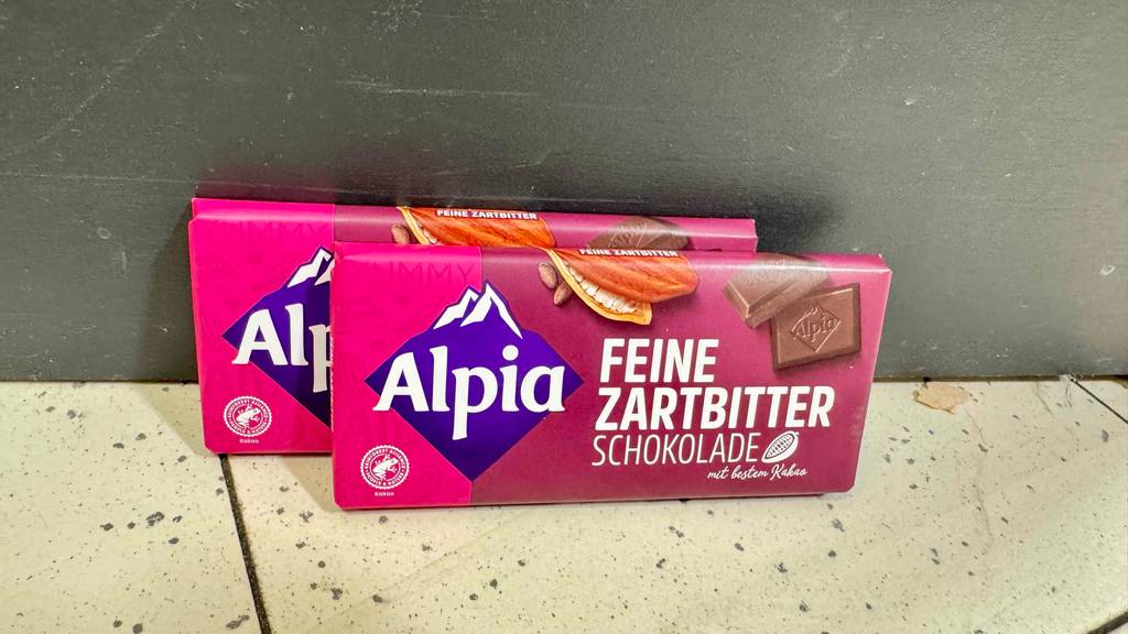 Zwei Tafeln getestete Alpia-Schokolade lehnen hintereinander an eine Wand.