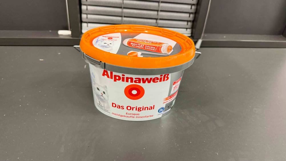 Auf einer grauen Fläche steht die getestete Alpina-Farbe.