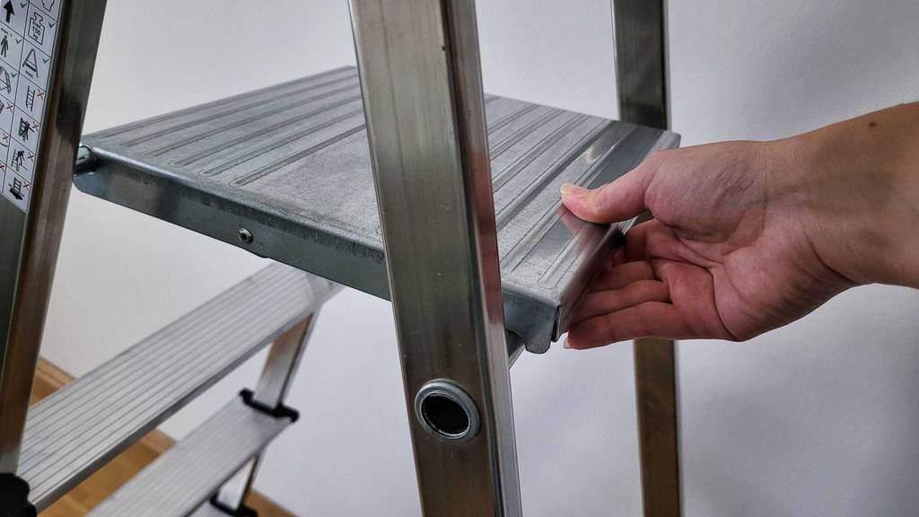 Im Test: Eine Hand klappt eine Trittstufe einer Aluleiter herunter.