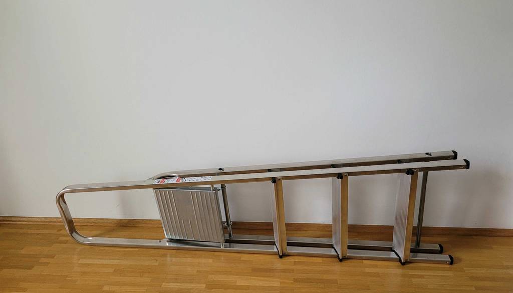 Eine Aluleiter liegt getestet auf der Seite vor einer weißen Wand.