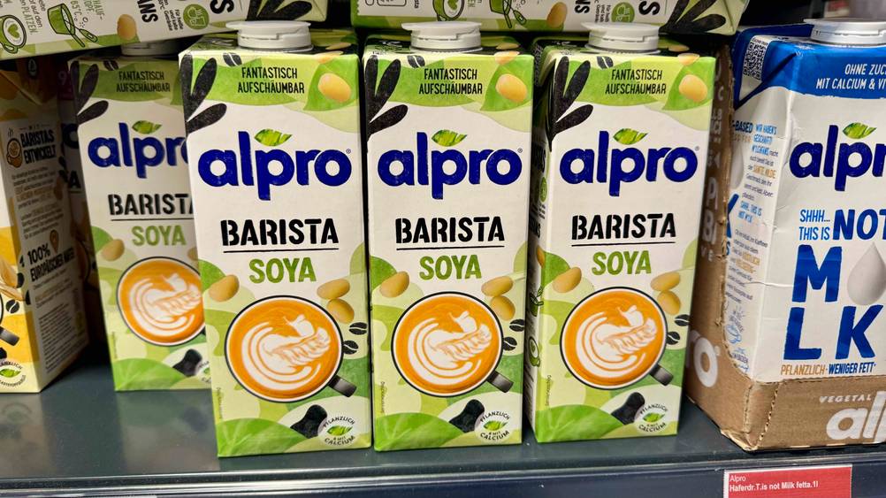 Mehrere Packungen der Alpro-Sojamilch im Test in einem Verkaufsregal neben anderen Produkten.