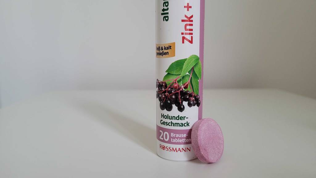 Nahaufnahme einer Dose mit Vitamin-C-+-Zink-Kapseln im Test, an die sich eine rosafarbene Brausetablette lehnt.