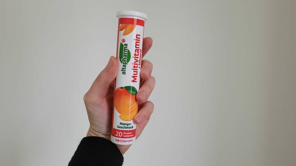 Eine Hand hält eine Dose mit getesteten Multivitamin-Brausetabletten vor einer weißen Wand.
