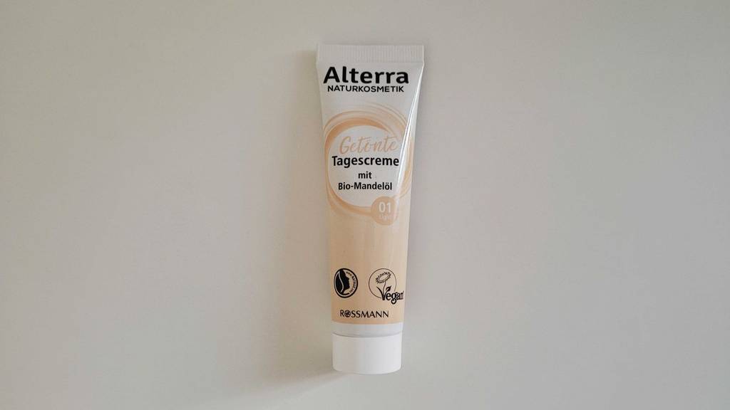 Weiß-beigefarbige Tube mit getönter Rossmann Alterra Tagescreme im Test, die sich auf einem weißen Untergrund befindet.