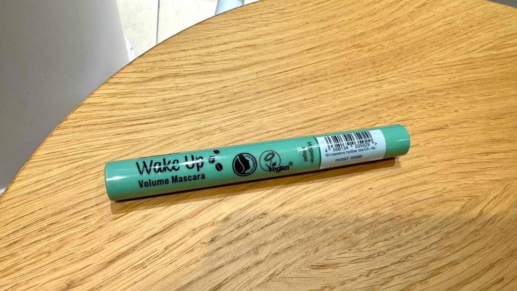 Ein getesteter veganer Mascara liegt auf einer Holzoberfläche.