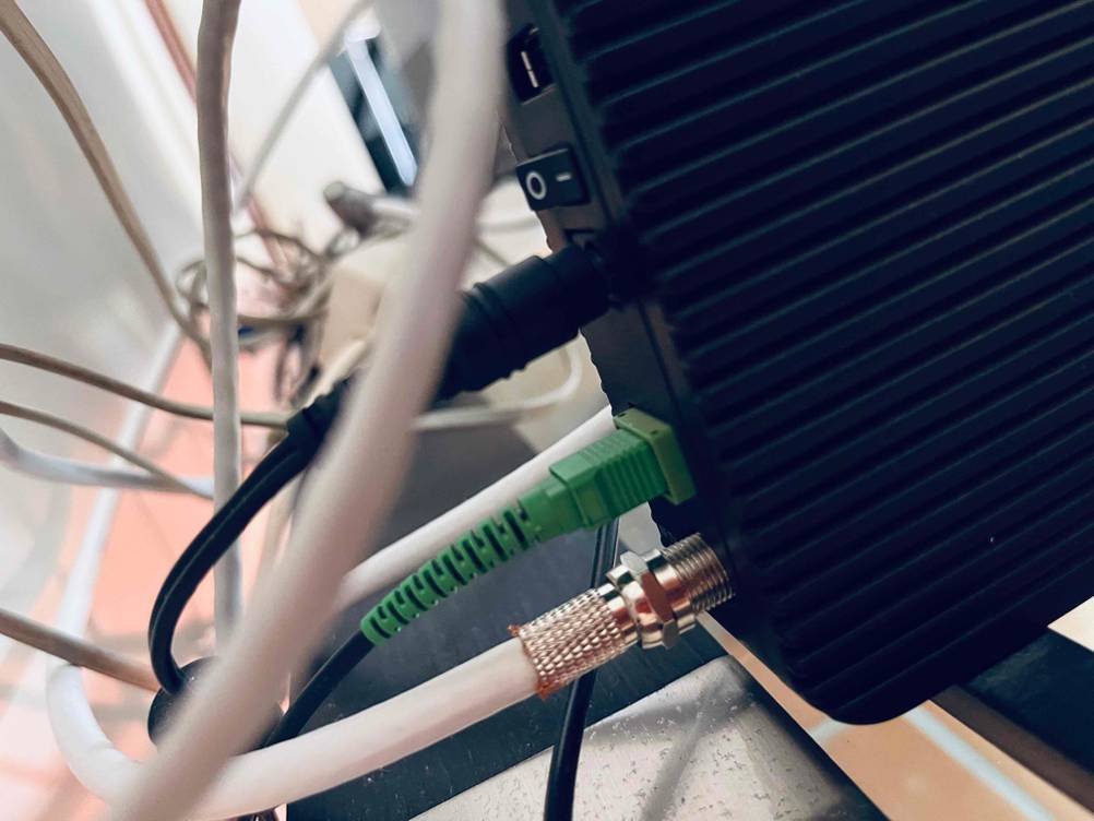 Detailaufnahme eines getesteten Glasfaser-Routers in Schwarz mit Fokus auf drei Anschlusskabel und den Einschaltknopf.
