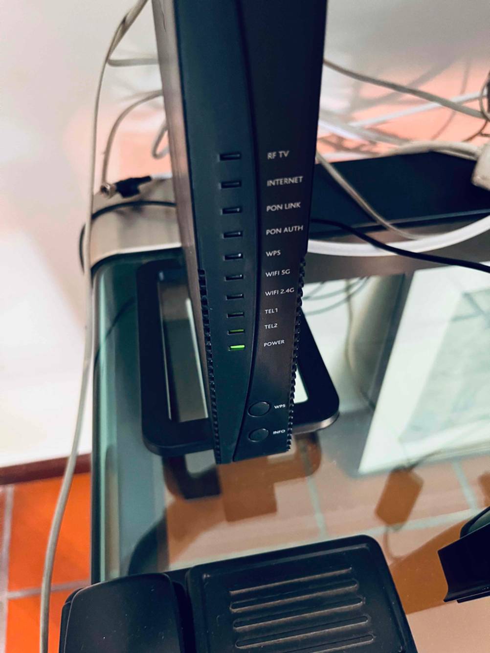 Ansicht von vorn der LED-Anzeigen eines schwarzen getesteten Glasfaser-Routers, der auf einem Glasschreibtisch steht.