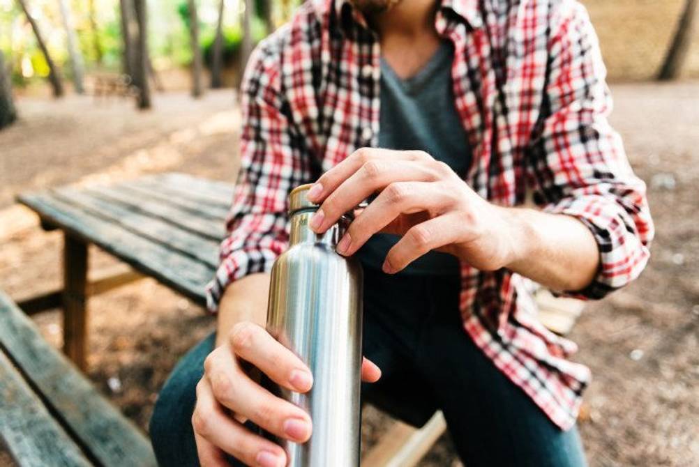Emsa-Isolierflaschen-Test: Outdoor-Enthusiast sitzt mit einer Isolierflasche auf einem Picknicktisch. 