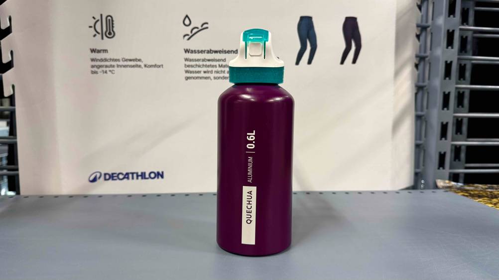Getestet: Eine Alu-Trinkflasche auf einer grauen Fläche vor einem Plakat.