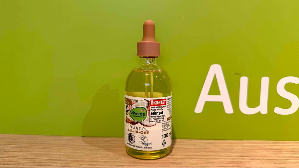 Eine Flasche Alverde-Gesichtspflege steht zum testen auf einem Holzbrett vor einem grünen Hintergrund.
