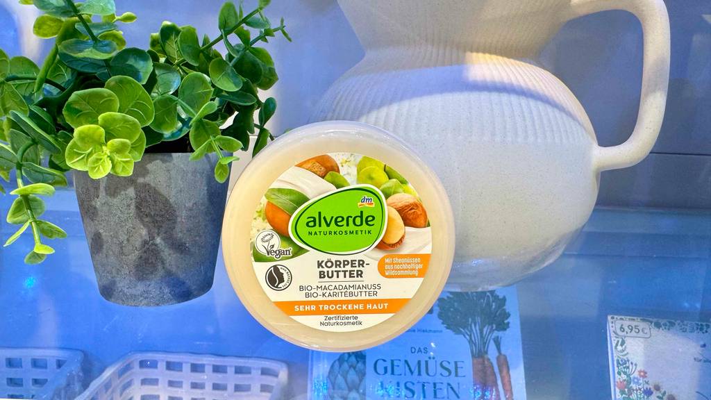 Getestet: Körperbutter in der Dose der Marke Alverde steht auf einem Glasregal neben einer Grünpflanze im Topf.