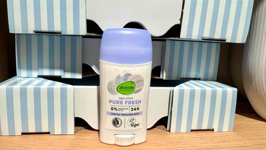 Ein Behälter mit Naturkosmetik-Deo steht zum testen vor gestreiften Kartons.