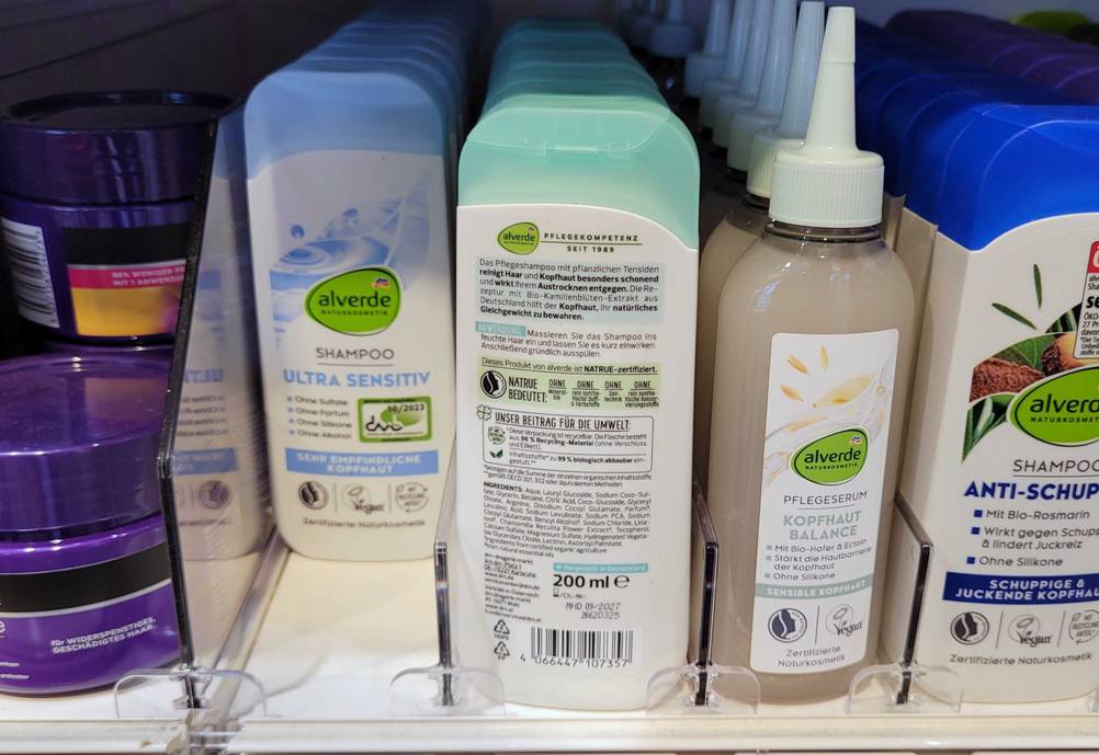 In einem Regal stehen mehrere Flaschen des alverde-Shampoo im Test die vorderste mit der Rückseite nach vorne.