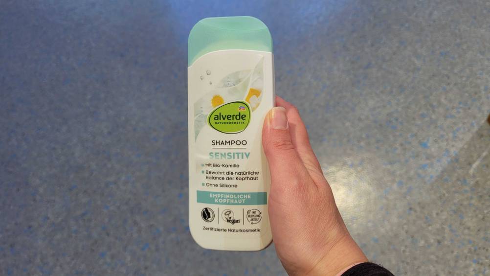 Eine Hand hält das getestete alverde-Shampoo hoch.